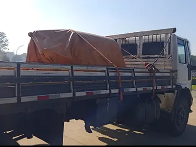 Caminhão de transporte rodoviário com equipamento coberto por lona e fixado com cintas de catraca